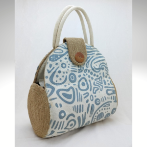 Handcrafted jute mini handbag with a natural beige texture and a white printed canvas front panel featuring a minimal blue-gray abstract pattern. The bag has soft, integrated double handles and a structured rounded silhouette.