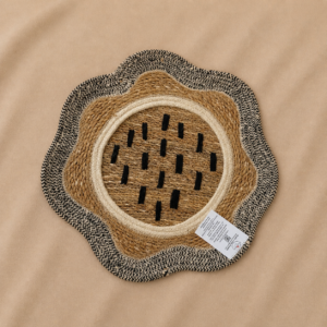 Handcrafted flower-shaped decorative tray made from natural jute and cane fibers, featuring a woven center, cream circular border, black accent marks, and wavy black-and-natural outer edge.
