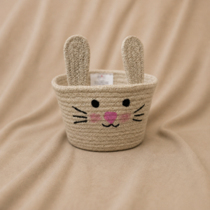 Handcrafted natural jute round storage basket with open top, upright bunny ears, black whiskers and eyes, pink nose and cheek details, and textured woven fiber finish.