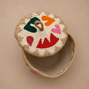 Handcrafted natural jute round storage basket with removable lid, loop handle, rope-style edging, and colorful heart and abstract artwork on the top