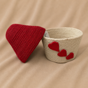 Handcrafted natural jute round storage basket with cream woven body, removable red fitted lid, and red heart appliqué details on the side.