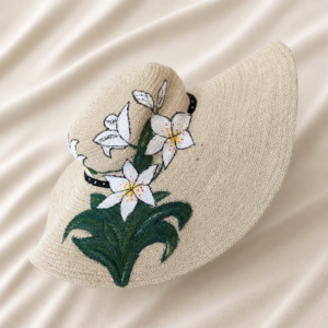Handcrafted natural jute wide brim sun hat featuring hand-painted white lily flowers, green leaves, black accent details, and textured woven beige fiber finish.