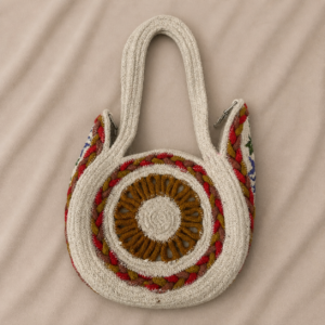 Handcrafted round jute handbag with circular mandala-style front design, colorful woven accents, double jute handles, metal clip details, zipper closure, and lined interior.